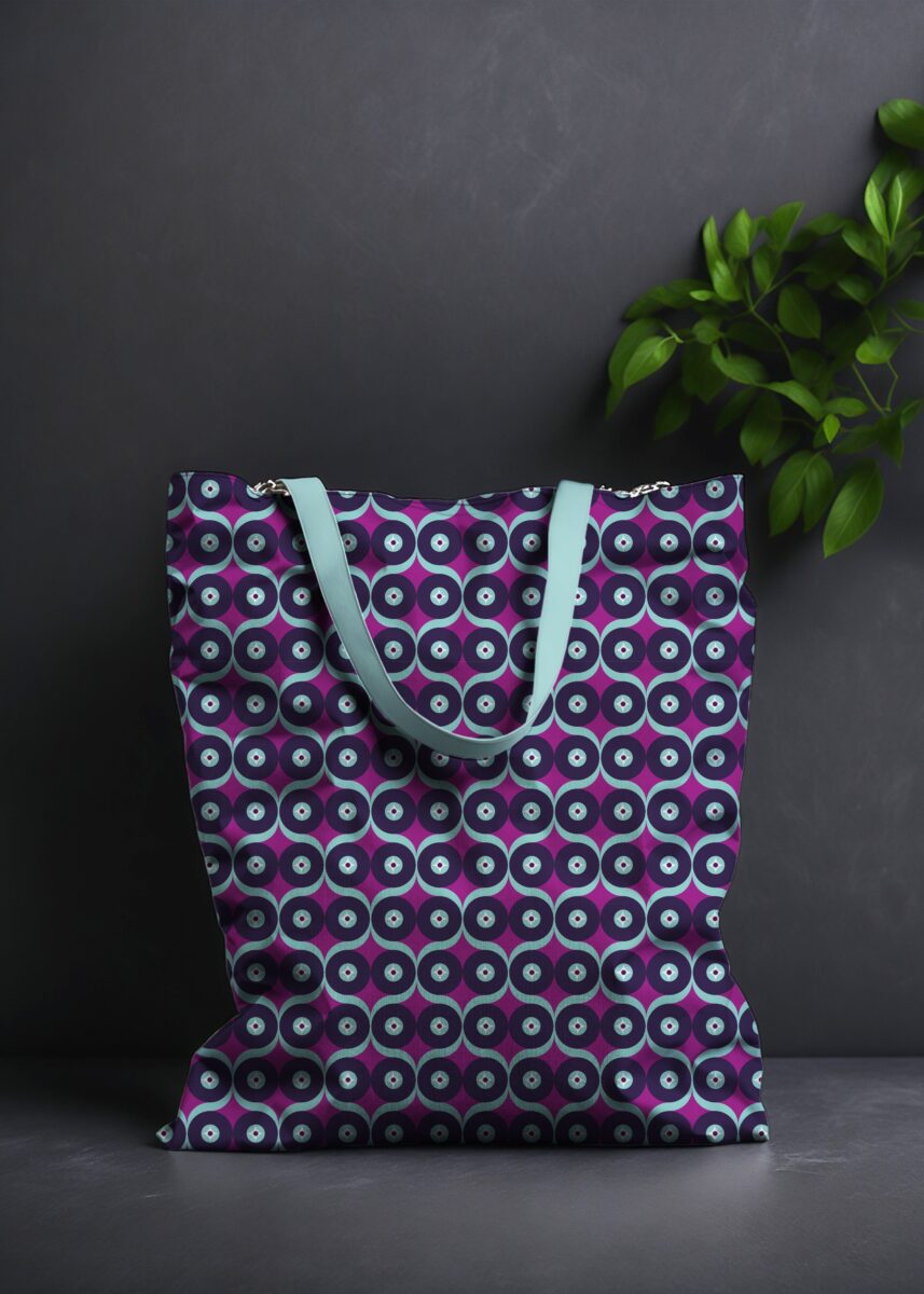Stoffdesign von Vandyra Design. Tasche mit geometrischem Eulenmuster. Die Farben auf dem Muster sind Mint, Plump, Indigo und Weiß. Der Hintergrund ist dunkelgrau und als Deko sieht man eine Pflanze zum Teil abgebildet.
