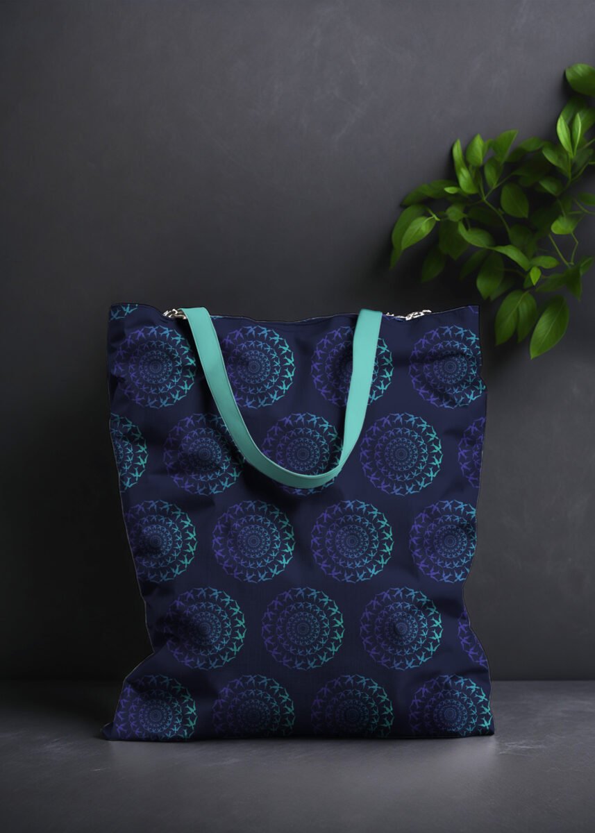 Stoffdesign. Tasche mit Vogelmuster. Motiv eines Vogelschwarm im Kreis. Das Muster ist Mint-Blau-Mitternachtsblau. Der Hintergrund ist dunkelgrau und als Deko sieht man eine Pflanze zum Teil abgebildet.