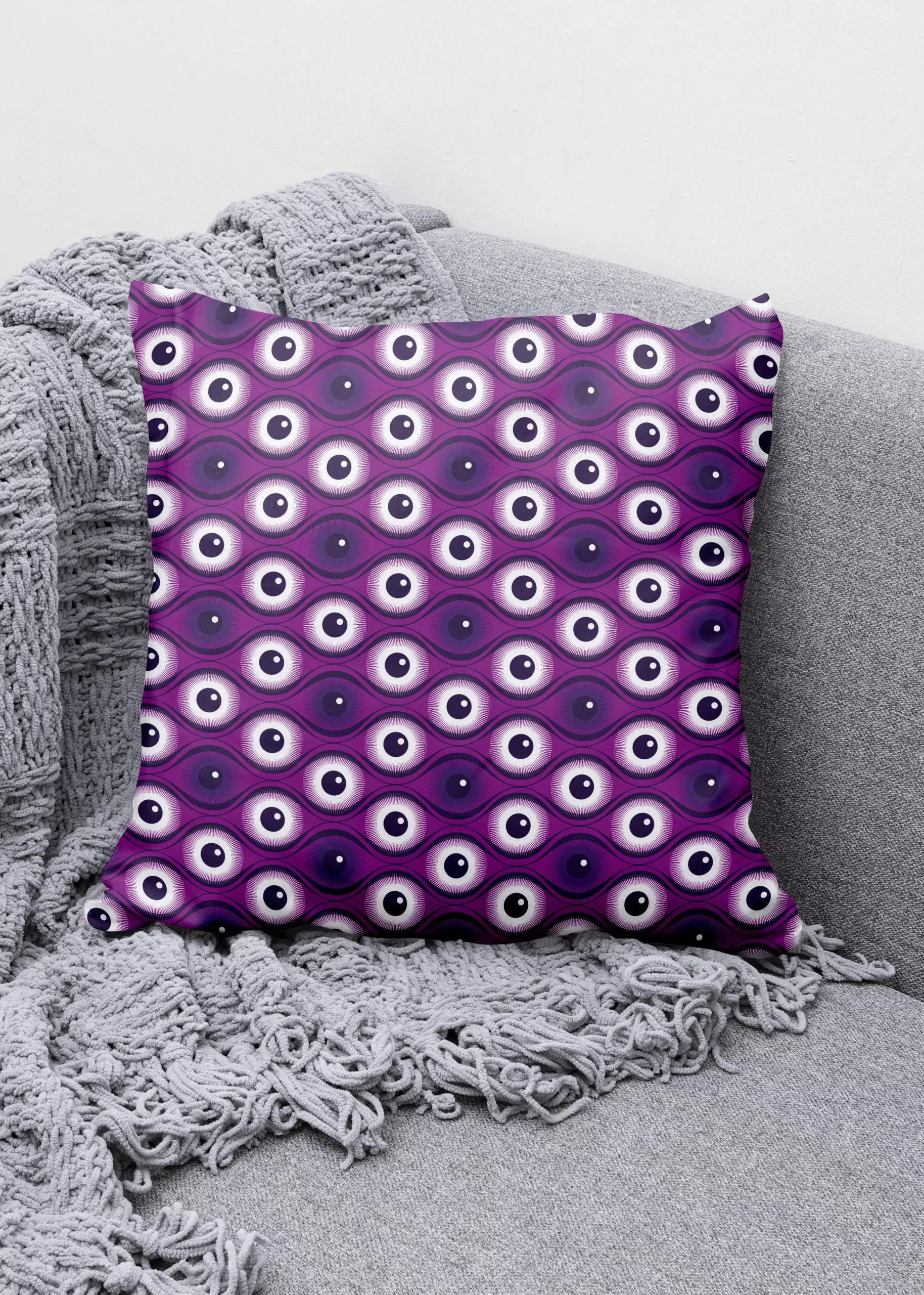 Stoffdesign von Vandyra Design. Ein Kissen mit einem geometrischen Augenmuster in Lilatönen und Weiß. Der Bildhintergrund ist ein helles Grau.