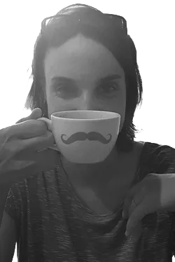 Portrait der Designerin Vandyra Design. Sie hält eine Kaffeetasse mit Schnurrbart über ihr Gesicht.