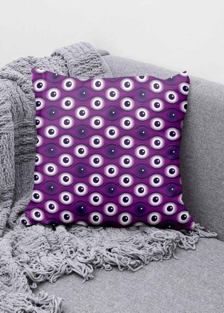 Stoffdesign von Vandyra Design. Ein Kissen mit einem geometrischen Augenmuster in Lilatönen und Weiß. Der Bildhintergrund ist ein helles Grau.