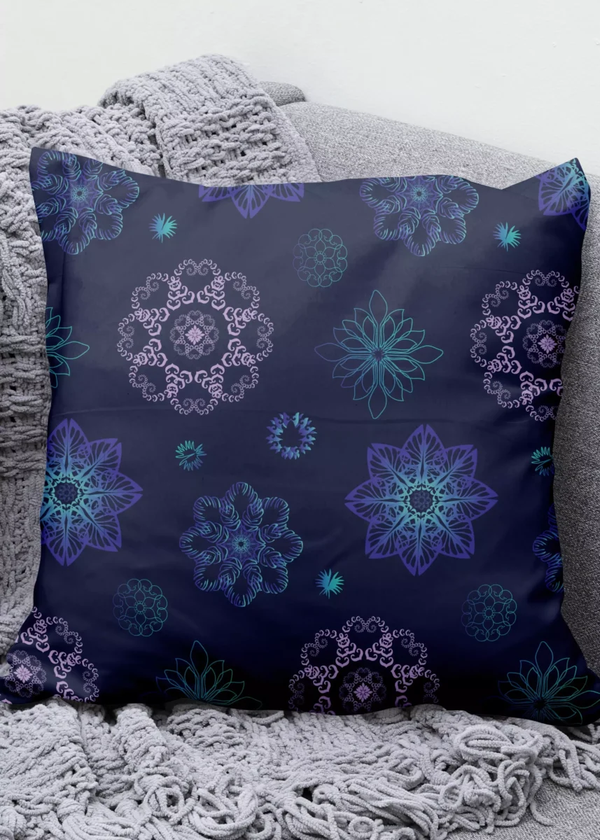 Stoffdesign von Vandyra Design. Mitternachtsfantasieblumen sind auf ein Kissen zu sehen, in rosa, türkis und hellblauen Farben mit teilweisen Farbverlauf. Der Hintergrundstoff ist ein tiefes Nachtblau. Dieses Kissen liegt auf einem grauen Sessel mit einer grauen Fransendecke.