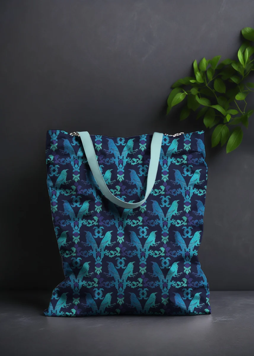 Stoffdesign von Vandyra Design. Tasche mit floralen und mystischen Krähendesign in Hellblau/Mint und Lila - Farbverlauf. Hintergrund ist ein dunkles Grau und als Deko sieht man eine Pflanze.
