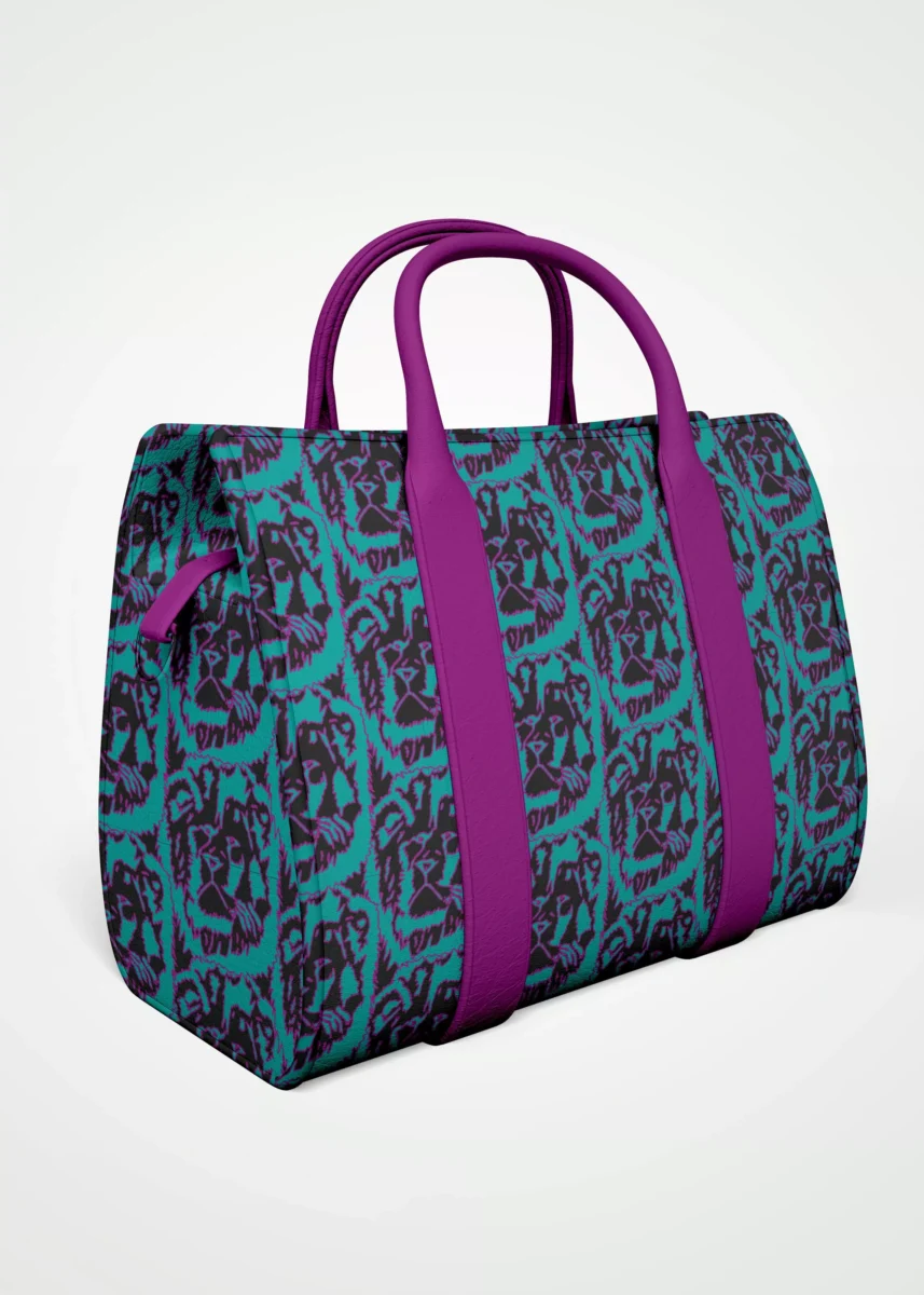 Stoffdesign von Vandyra Design. Eine Tasche mit einem handgezeichneten tierischen Löwenkopf - Muster. Die Farben sind Fuchsia und Türkis und der Hintergrundstoff ist Schwarz. Die Henkel der Tasche sind in Fuchsia und aus Kunstleder. Die Tasche wird etwas seitlich dargestellt. Der Bildhintergrund ist ein helles Grau.