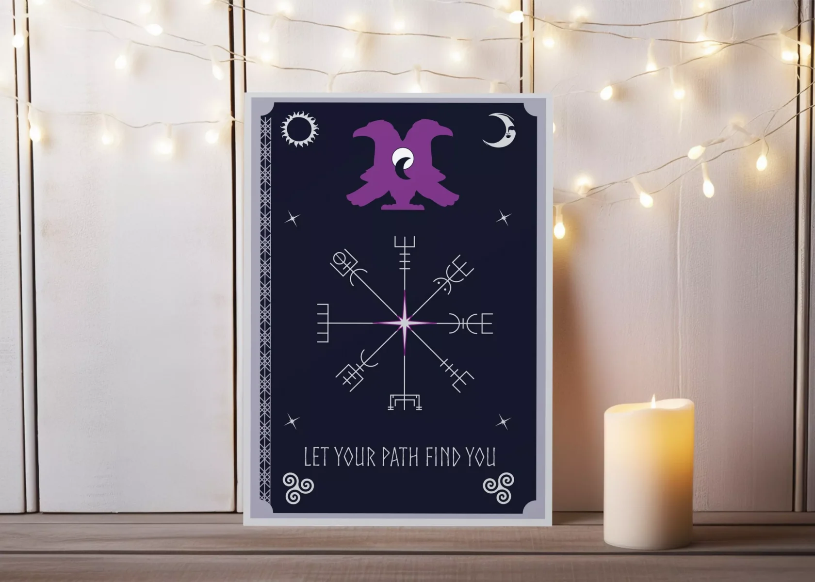 Postkartendesign von Vandyra Design. Auf dieser sieht man mystische Symbole Sonne, Mond, Sterne, stilisierte Vögel (Hugin & Munin) und in der Mitte das Vegvísir als Wegweiser in silber. Als Text steht in Silber drunter: "Let your path find you". Der Hintergrund ist Mitternachtsblau. Als Deko auf dem Bild, wo die Postkarte abgebildet ist sieht man eine brennende Kerze.