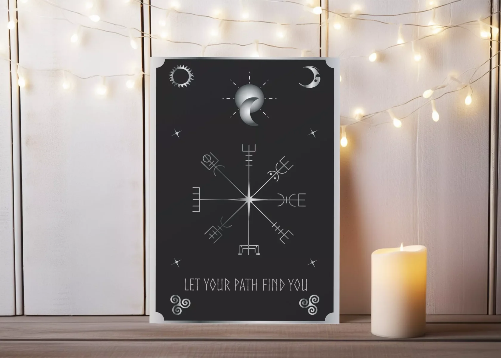 Postkartendesign von Vandyra Design. Auf dieser sieht man mystische Symbole Sonne, Mond, Sterne und in der Mitte das Vegvísir als Wegweiser in silber. Als Text steht in Silber drunter: "Let your path find you". Der Hintergrund ist Grau-Schwarz. Als Deko auf dem Bild, wo die Postkarte abgebildet ist sieht man eine brennende Kerze.