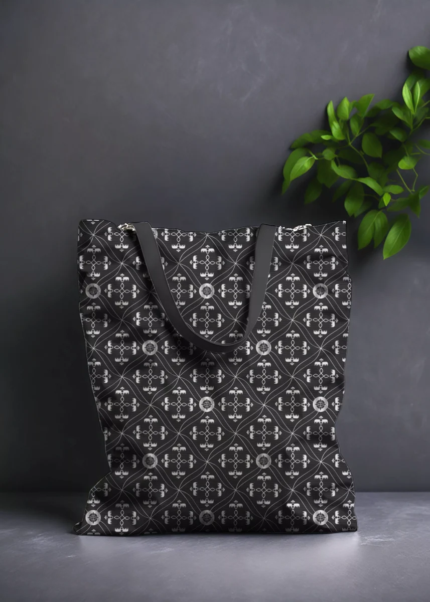 Stoffdesign von Vandyra Design. Tasche mit Motiven vom abstrahierten Drachen im Flug - Fantasiemuster in silbernen glänzenden Farbverlauf mit schwarz-grauen Hintergrund. Der Stoff ist leicht verzwirbelt. Hintergrund ist ein dunkles Grau und als Deko sieht man eine Pflanze.